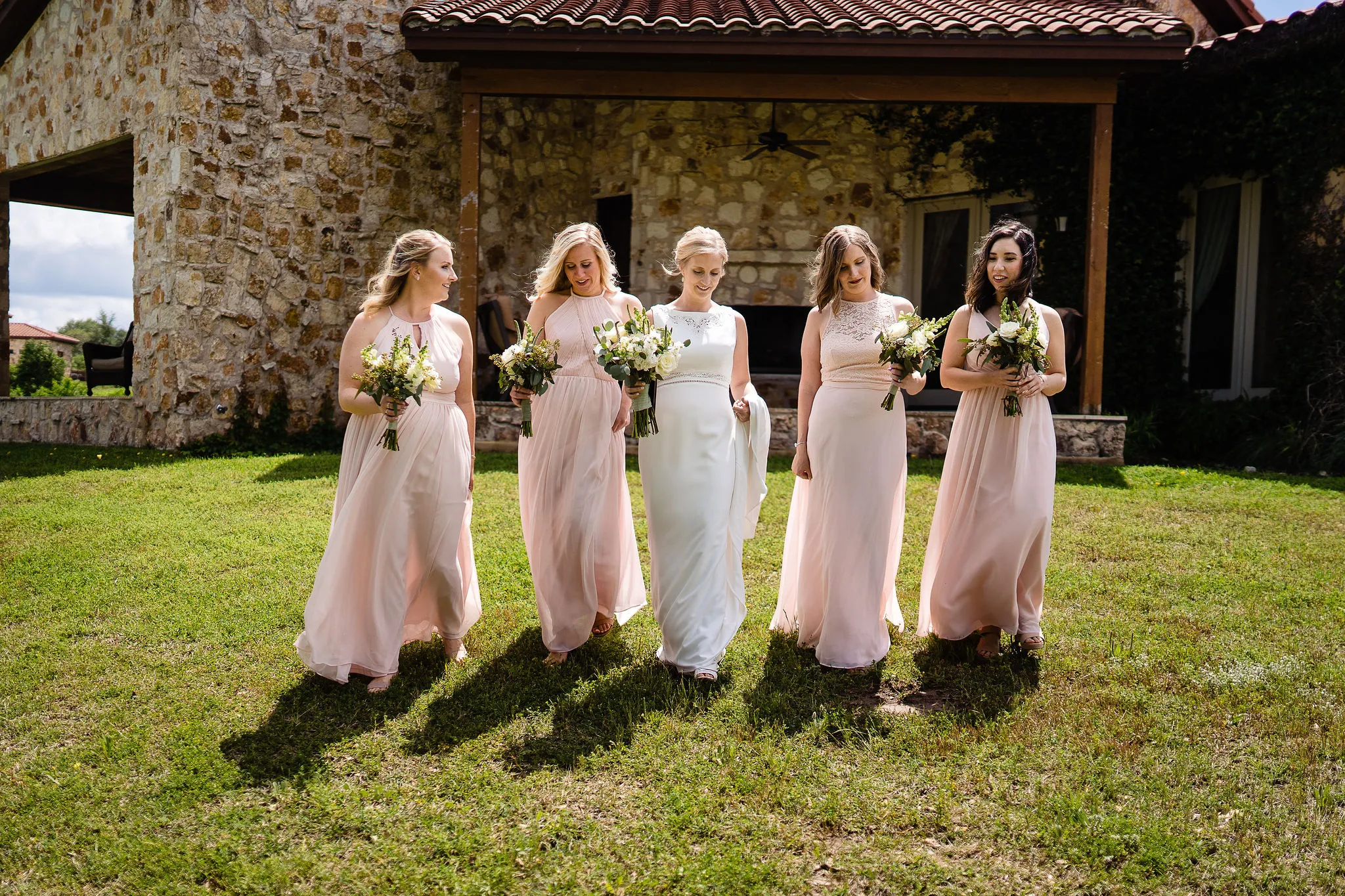 a bride walks alongside her bridesmaids wearing light pink dresses