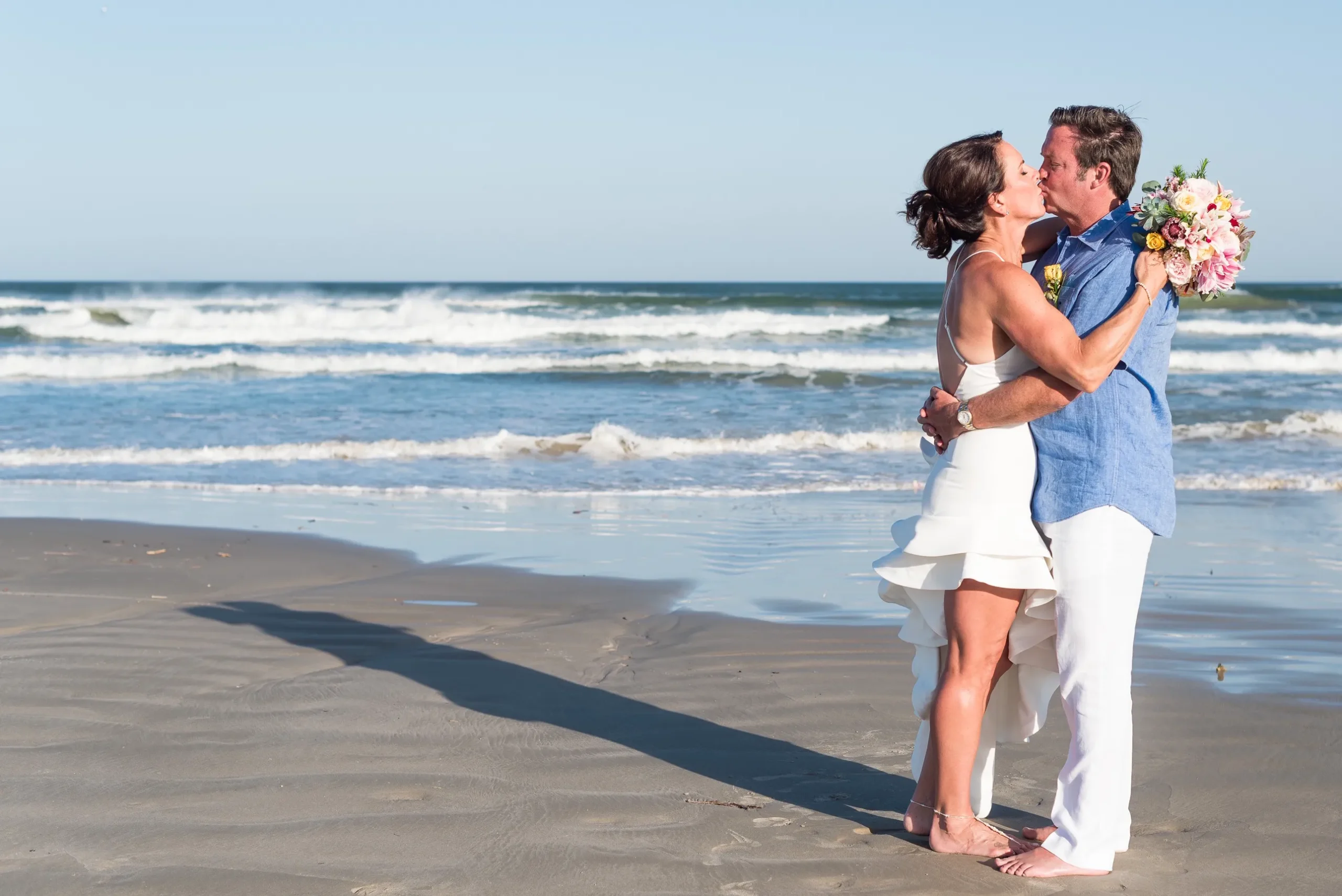 a bride and groom pose on a beach