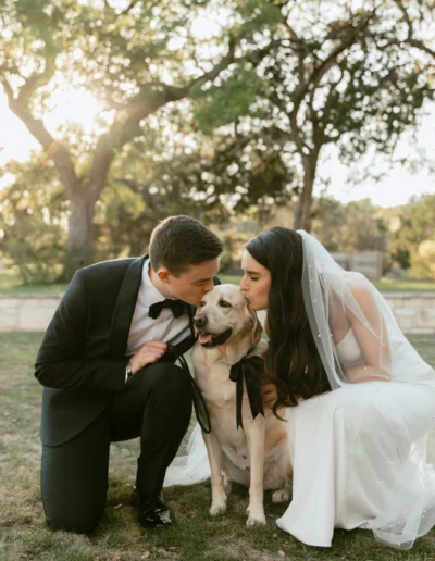 a bride and groom kneel by their pet dog for their wedding day