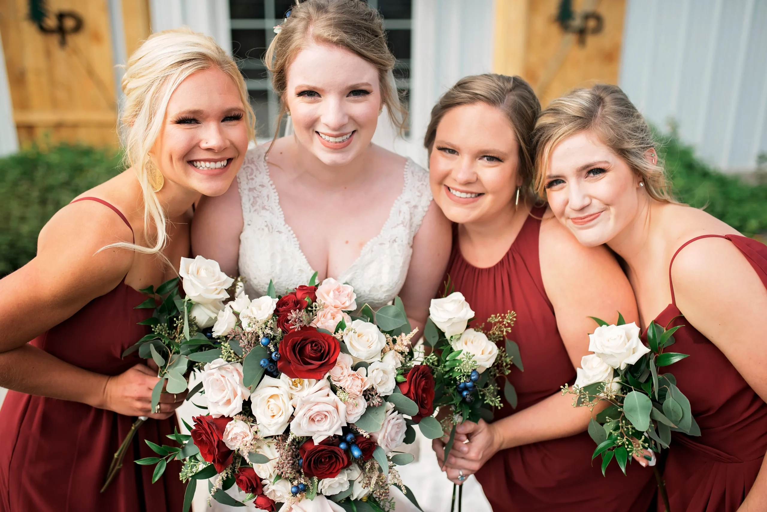 a bride poses with her bridesmaids who wear red dresses