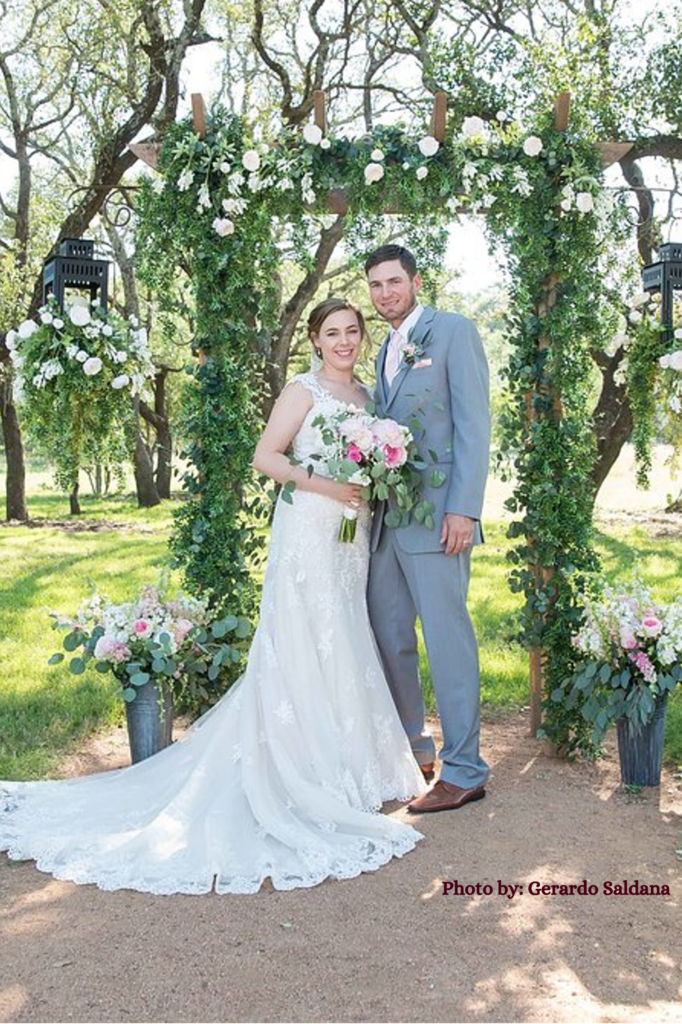 A married couple poses in front of their wedding ceremony arch