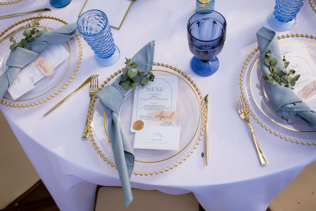 Beautiful gold rimmed glass plates set with a blue cup for a wedding reception.