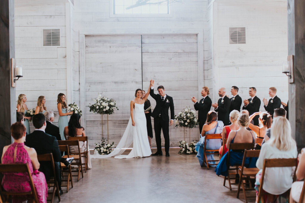 A wedding ceremony organized by a wedding planner with the bride and groom raising their hands in the air with joy.