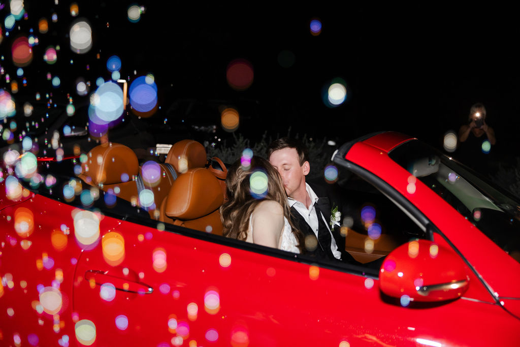 A couple kisses in a red convertible after their wedding day